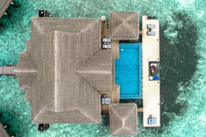 Stunning aerial view of a luxury villa with a swimming pool in the Maldives over turquoise waters.