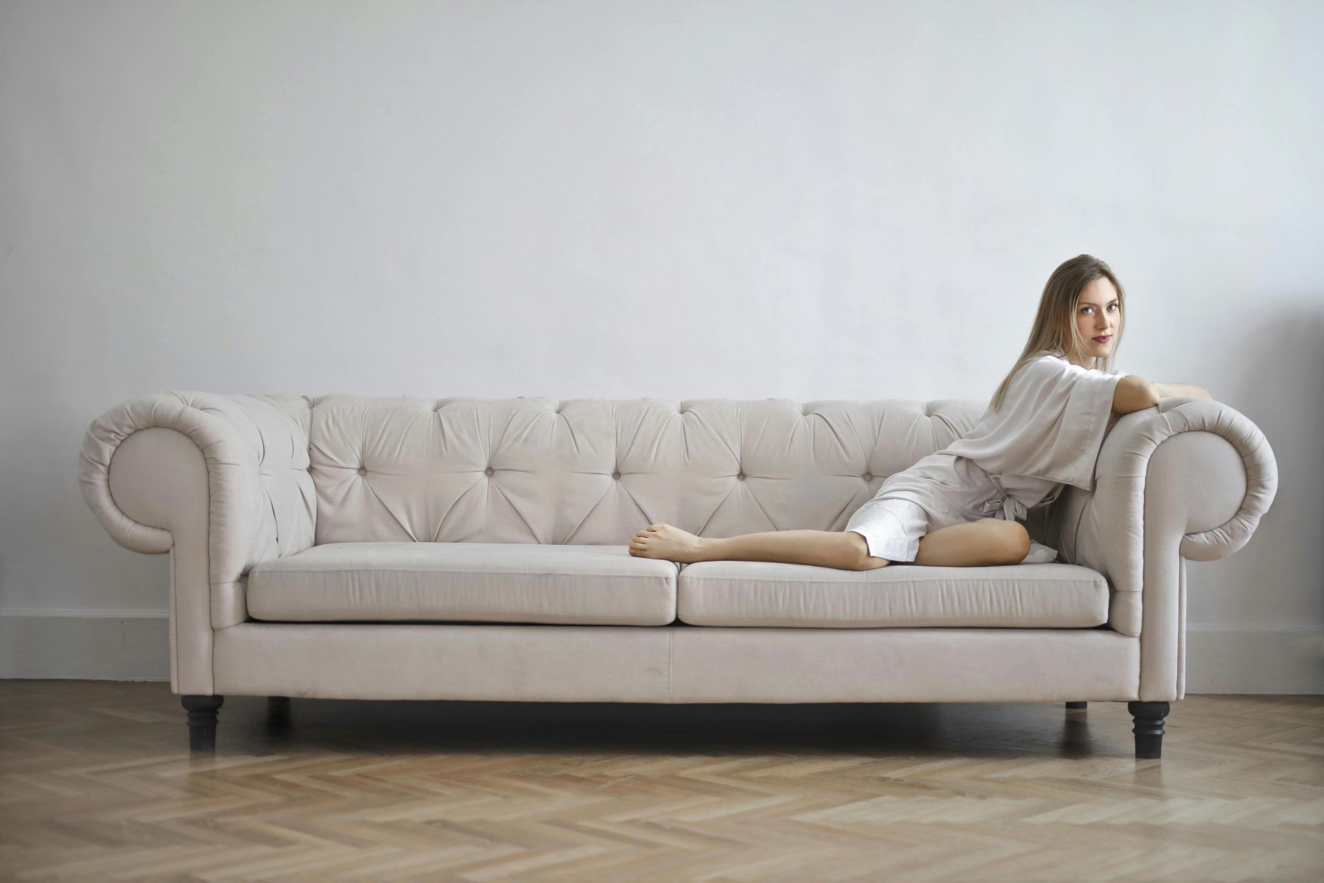 Elegant woman in silk robe reclining on a white sofa indoors, exuding calm and sophistication.